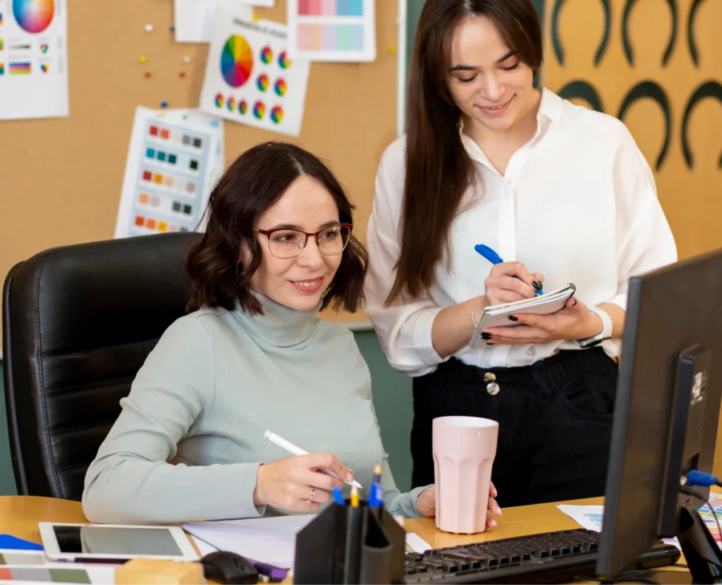 Two young lady colleagues taking notes from the desktop