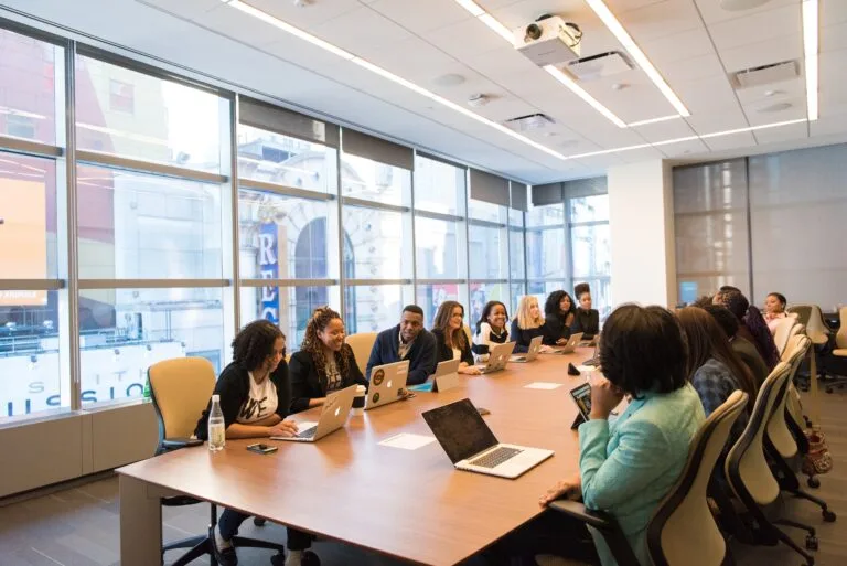 Diverse group of professionals engaged in a meeting around a conference table with laptops.