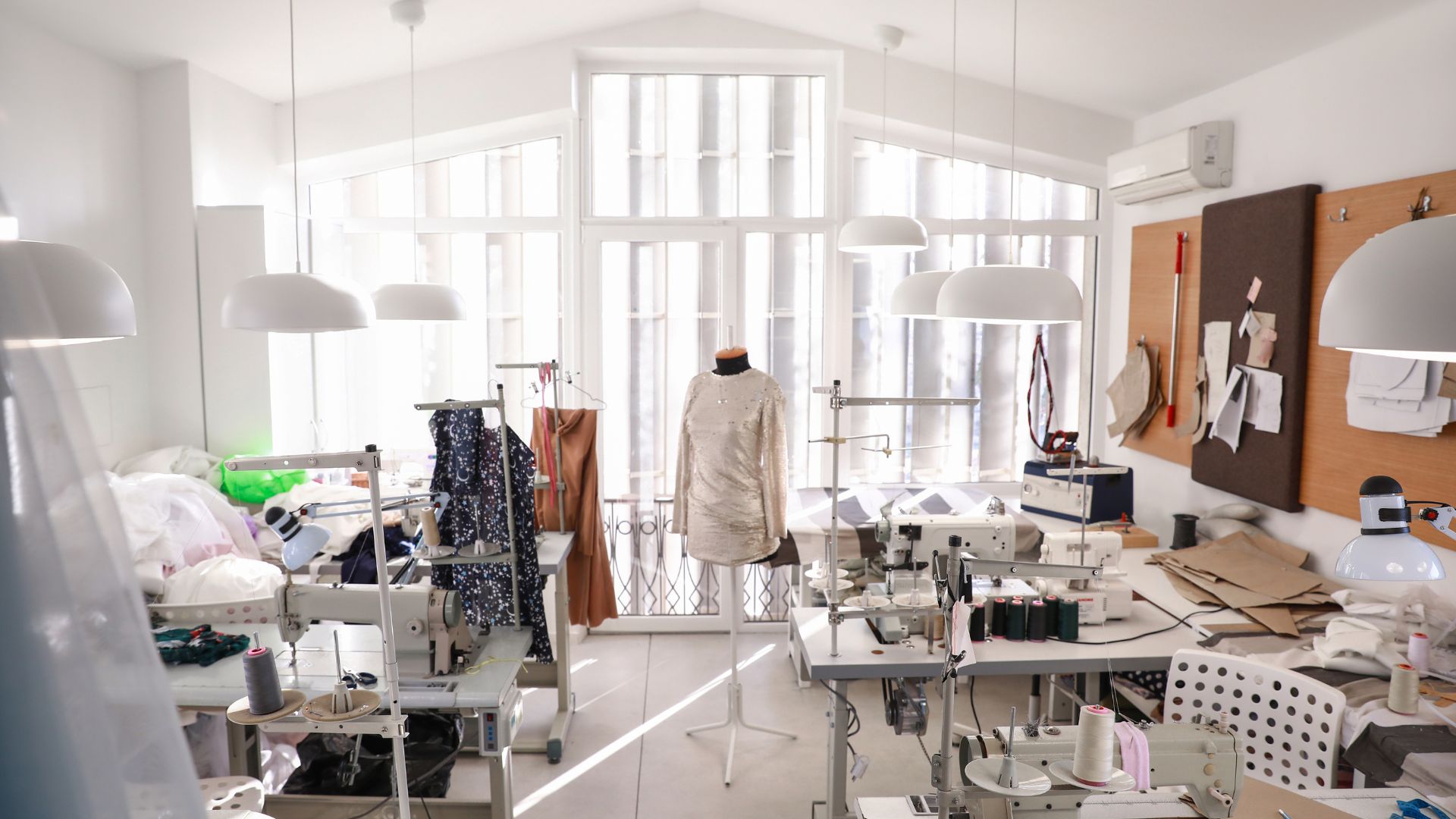 A well-lit apparel manufacturing workspace with sewing machines, fabric rolls, and a mannequin displaying a garment.